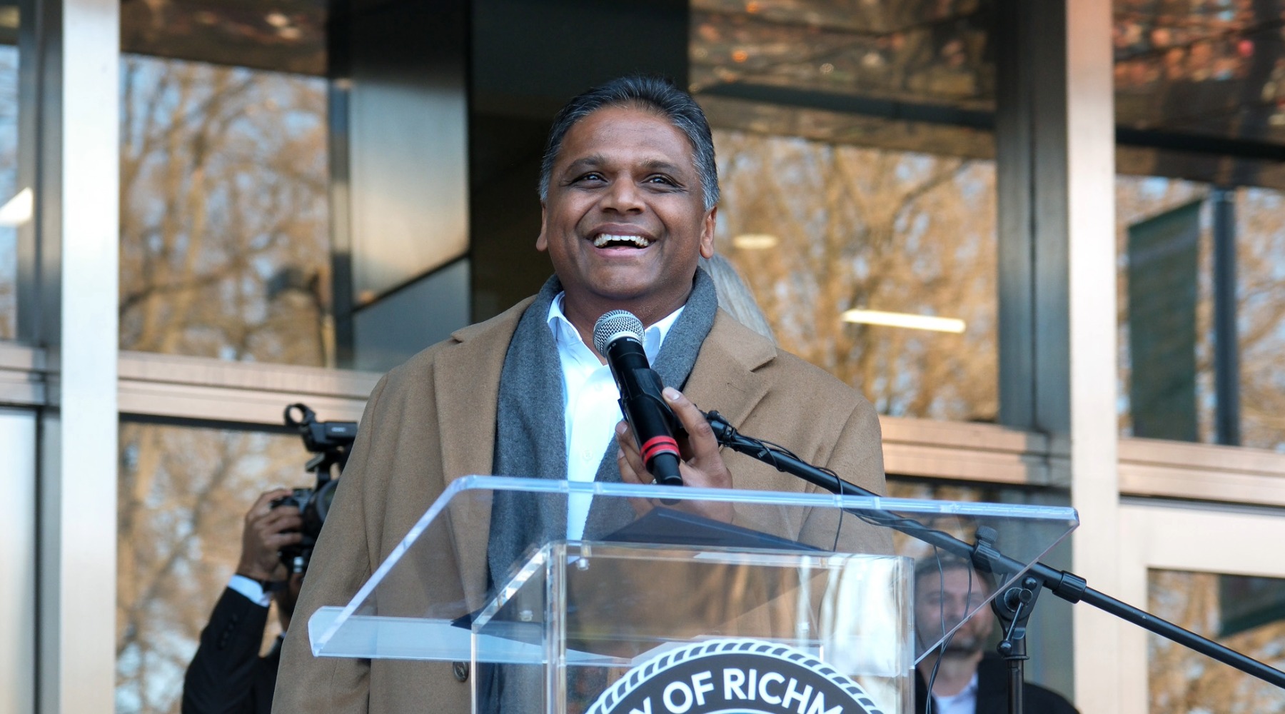 Mayor Danny Avula at a podium wearing a brown coat