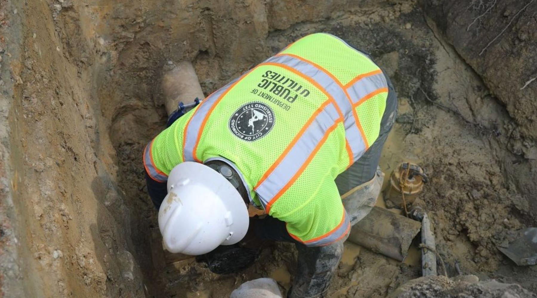 A worker in a bright green public utilities vest repairs an underground pipe.