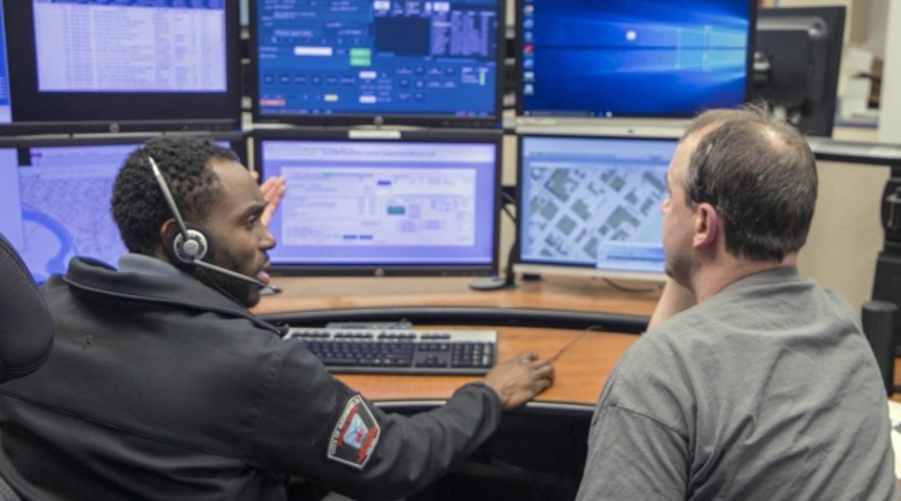 A 911 operator and staff member talk in front of several computers.