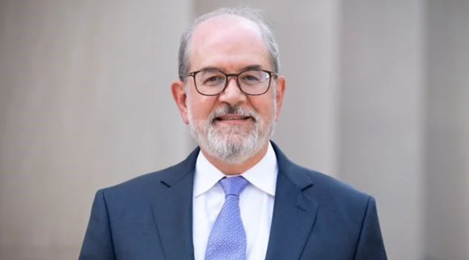 Judge Jewett in a blue suit with a light blue tie and glasses in front of a white background